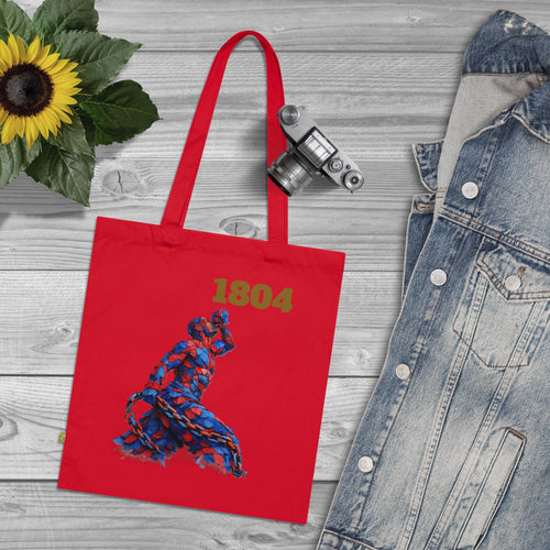 Red tote bag with '1804' and a dancer design, placed on a wooden surface with a sunflower and denim jacket.