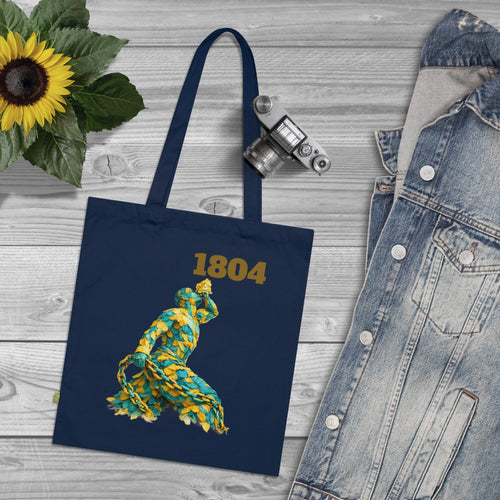 Navy tote bag with '1804' and bear design, sunflower, camera, and denim jacket on wooden surface