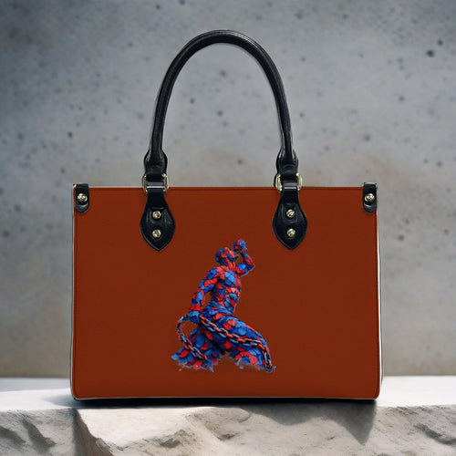 Brown handbag with black handle and blue and red embroidered design on a textured surface.